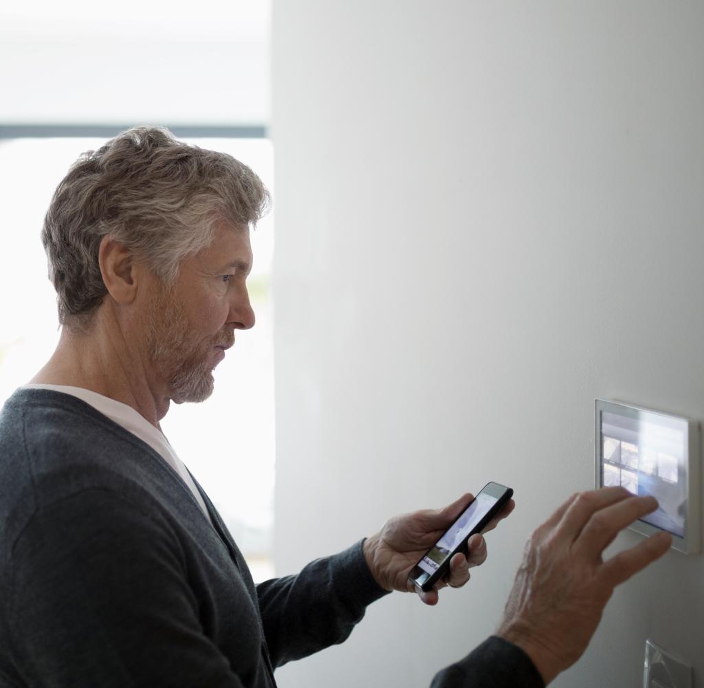 Senior man using smart phone app, adjusting digital thermostat